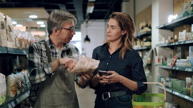 Video of  pretty young woman shopping while the seller advises on her purchases of organic food in a grocery store.