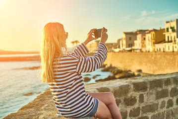 Woman traveler tourist using smartphone, taking photo of sea view at sunset in summer day. Enjoying European, Famous popular touristic place in world.