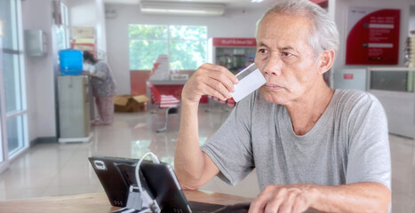 Fototapeta na wymiar An elderly Asian man sitting in front of a tablet holding a bank card.