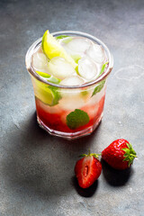 cold detox water with lime, strawberry, mint in the glass with ice cubes on gray background