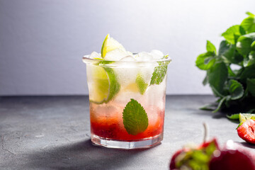 cold detox water with lime, strawberry, mint in the glass with ice cubes on gray background. copy space