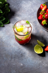 cold detox water with lime, strawberry, mint in the glass with ice cubes on gray background. copy space