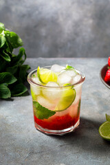 cold detox water with lime, strawberry, mint in the glass with ice cubes on gray background