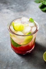 cold detox water with lime, strawberry, mint in the glass with ice cubes on gray background. close up