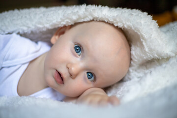 smiling baby looking at camera under a white blanket, towel. selective focus