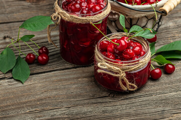 Fresh red cherries fruit on wooden background. Jar of cherry jam and sour cherries. Berries cherry with syrup. Canned fruit. place for text, top view