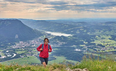 nice senior woman hiking at Mount Gruenten in the Allgaeu Alps with awesomw view over Iller valley to Lake Alpsee and Lake of Constanz, Bodensee,  Bavaria, Germany