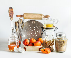 Baking setting with apricots and kitchen utensils at white background. Front view.