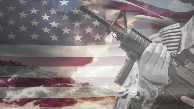 Animation of hand of soldier holding gun over waving american flag and cloudy sky