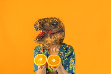 Woman in dinosaur animal head mask showing fresh orange slices,isolated on orange...
