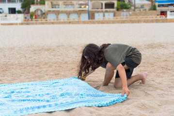 Image knee level, long shot of a boy with long hair laying his towel on the beach sand to sunbathe.sunbathe