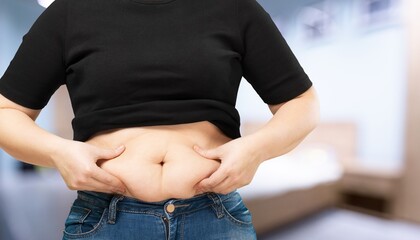 Young woman standing near bed in bedroom. Fat burning treatment of thick belly. Weight loss program, dieting.