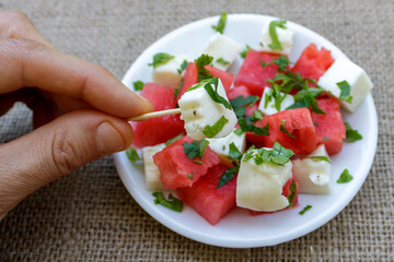 Close-up of plate of Cypriot traditional halloumi cheese and watermelon salad with hand