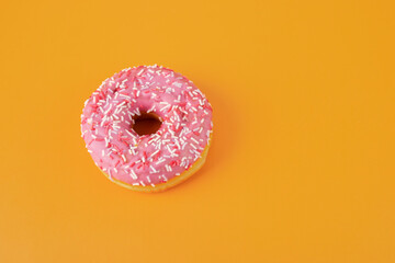 Fototapeta na wymiar pink glazed donut on orange background, copy space, sweets and pastries, harmful dessert