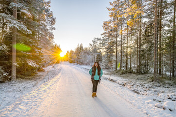 Fototapeta na wymiar A calm tranquil view of the snow covered trees in the snowdrifts and beautiful sunset. A beautiful woman in coloured jacket walking through the Magical winter forest.