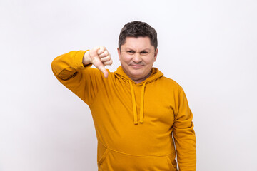 Middle aged man showing thumbs down, expressing disapproval, criticizing and disagreeing with suggestion, wearing urban style hoodie. Indoor studio shot isolated on white background.