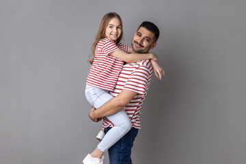Portrait of happy positive father and daughter in striped T-shirts standing looking at camera with...