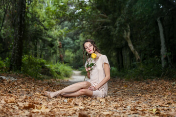 Young Woman Sitting And Holding A Yellow Rose In The Forest