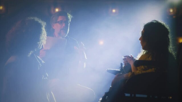 An actress with a disability and an actor rehearsing a performance on the theater stage illuminated by a spotlight with the director