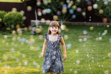 smiling child girl enjoying playing with soap bubbles outdoors on summer day. Cute kid child catches soap bubbles in nature. happy childhood concept