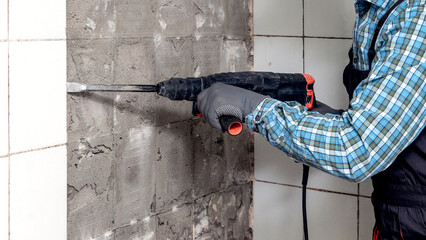 A builder uses a perforator to remove an old facing tile during a bathroom renovation