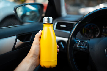 Close-up of male hand holding steel reusable water bottle of yellow, inside car.