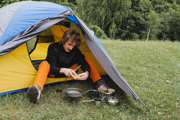 Fried scrambled eggs on a hike in a frying pan, a guy cooks in a tent, camping in nature, knife in...
