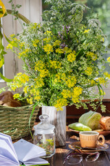 bouquet of wild flowers, mug of tea, eyeglasses and notebook on wooden table at summer morning