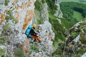 A man sits on the edge of a cliff looking into the distance, a guy enjoys the beauty of nature, hiking in the mountains, hiking with a backpack, time to relax