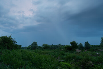 Summer storm with rain and lightning above channel overgrown with grass