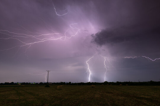 Thunderstorm above field with roll bales of hay at night, cloud to ground branched lightning, lightning in clouds at night in countryside - Powered by Adobe