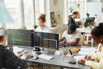 Group of programmers working in team with new project at table behind the window at office