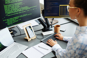 Female programmer typing codes to new software on computer while sitting at her workplace at office