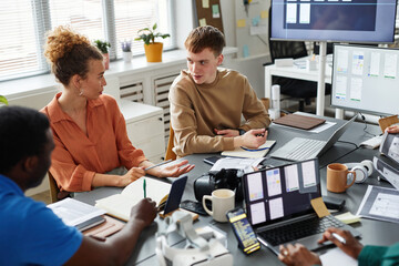 Obraz premium Team of programmers discussing and testing new software together at table during meeting at office