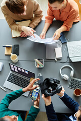 High angle view of team of developers developing new project with virtual reality glasses at table...
