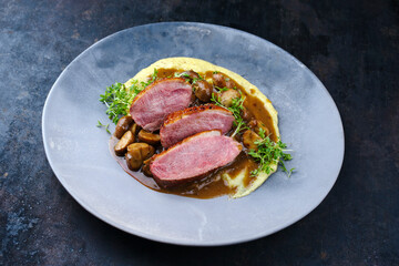 Barbecue gourmet duck breast filet with polenta and caramelized mushrooms in hearty beer sauce served as close-up in a design plate
