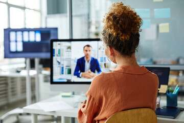 Rear view of businesswoman having online meeting on computer with her colleague while sitting at...