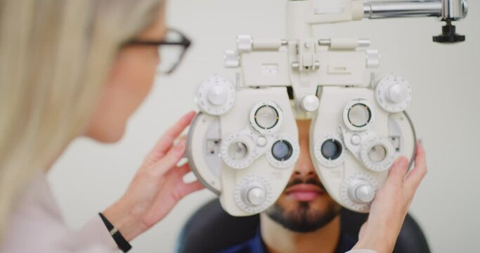 Optometrist using eye phoropter machine to examine patients refractor strength in clinic consult. Healthcare medical professional adjusting ophthalmic equipment, checking for astigmatism or myopia