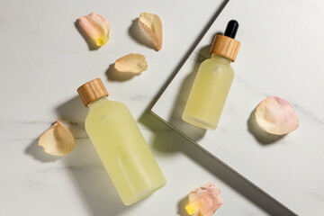 Bottles of essential oil and flower petals on white marble table, flat lay