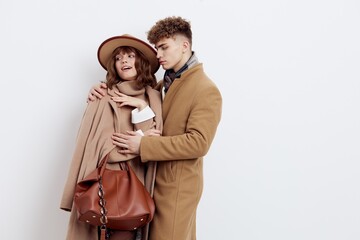 a cute couple in love a man and a woman in a stylish autumn rain stand hugging on a white background and a woman holds a brown bag in her hand
