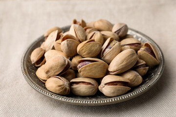 Plate with pistachio nuts on beige tablecloth, closeup