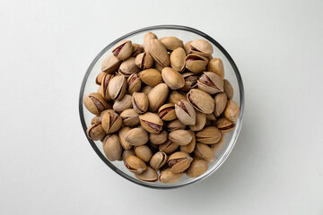 Bowl with pistachio nuts on white background, top view