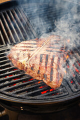 Barbecue dry aged wagyu porterhouse beef steak grilled as close-up on a charcoal grill with fire...