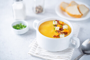 Potato carrot soup with fried bacon slices in a bowl