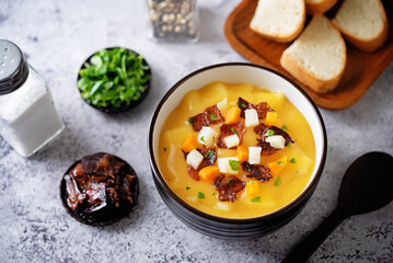 Potato carrot soup with fried bacon slices in a bowl
