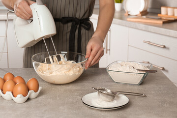 Fototapeta na wymiar Woman whipping white cream with mixer at light grey table in kitchen, closeup