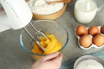 Fototapeta na wymiar Woman beating eggs with mixer at light grey table, closeup