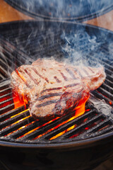 Barbecue dry aged wagyu porterhouse beef steak grilled as close-up on a charcoal grill with fire and smoke