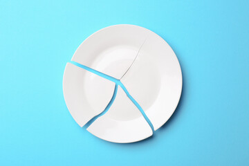 Pieces of broken ceramic plate on light blue background, flat lay