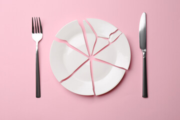 Pieces of broken ceramic plate and cutlery on pink background, flat lay